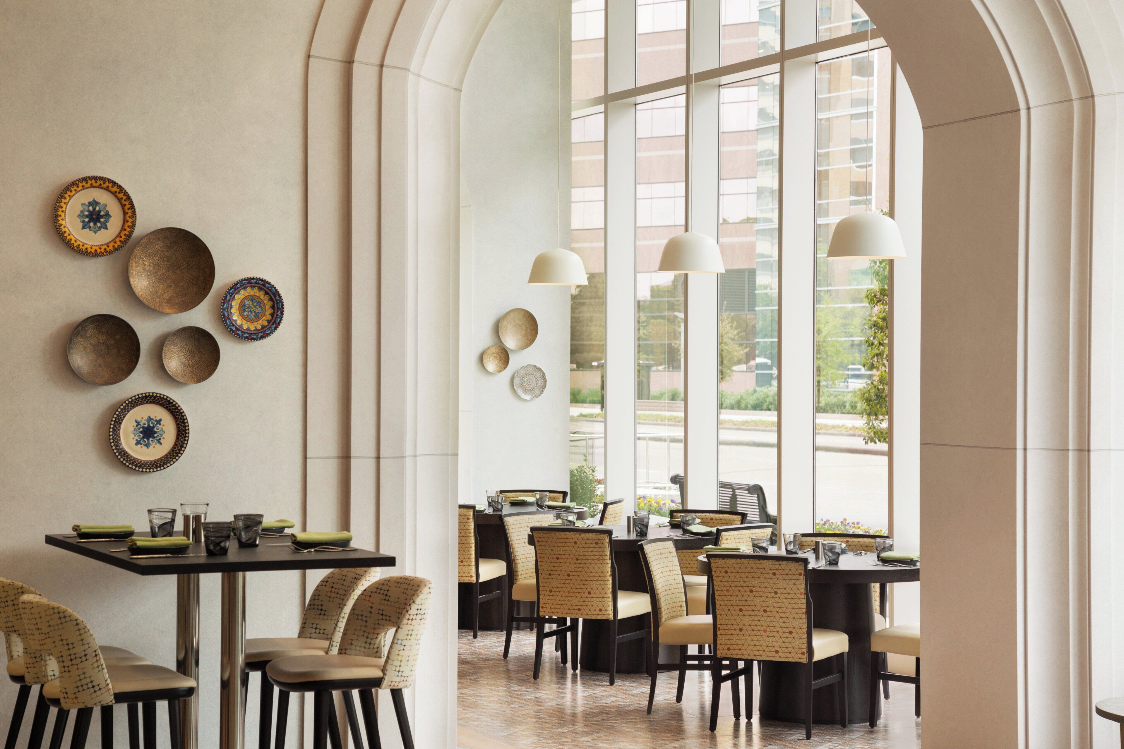 L’intérieur d’un restaurant se caractérise par de hauts plafonds, de grandes fenêtres et une variété de types de tables.
