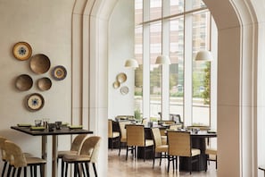 Un interior de restaurante con techos altos, grandes ventanales y diversas mesas dispuestas.