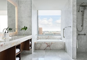 A modern bathroom with a large window, a bathtub, a shower, and a vanity with a mirror.