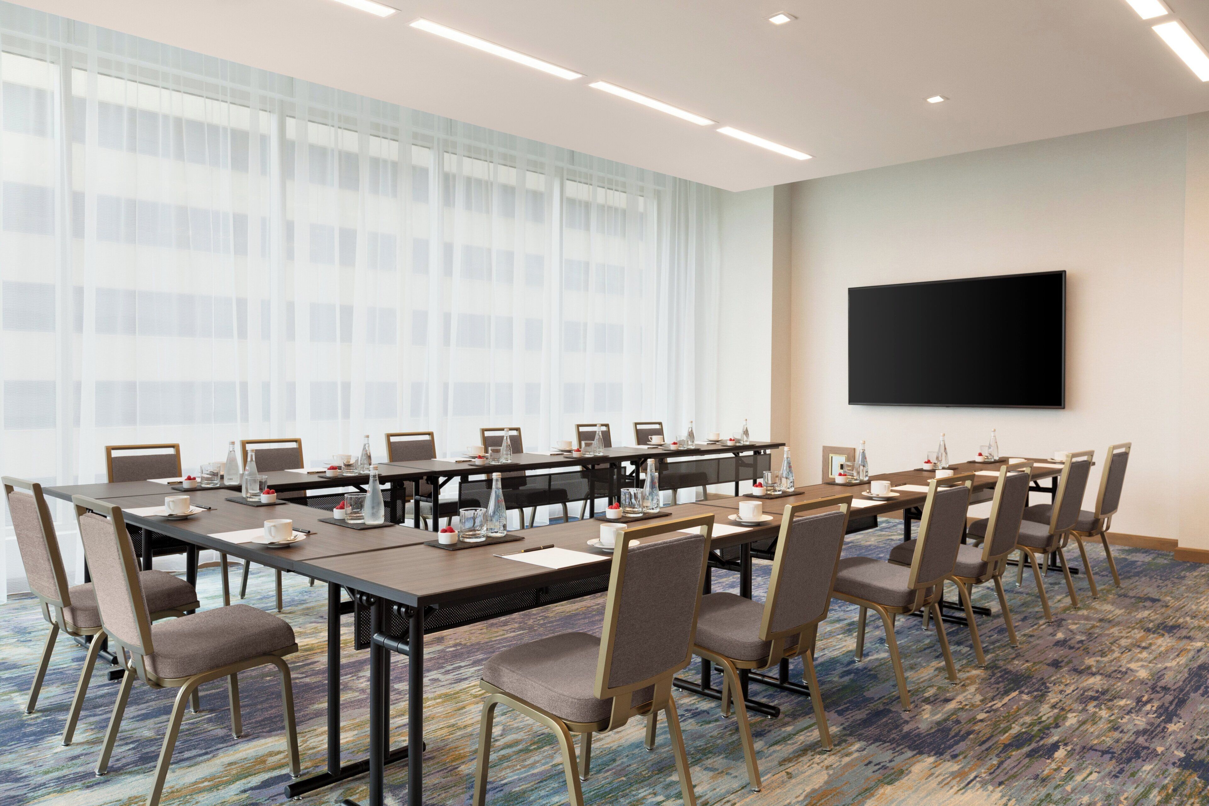 Une salle de conférence avec une longue table, des chaises et un téléviseur à écran plat fixé au mur.