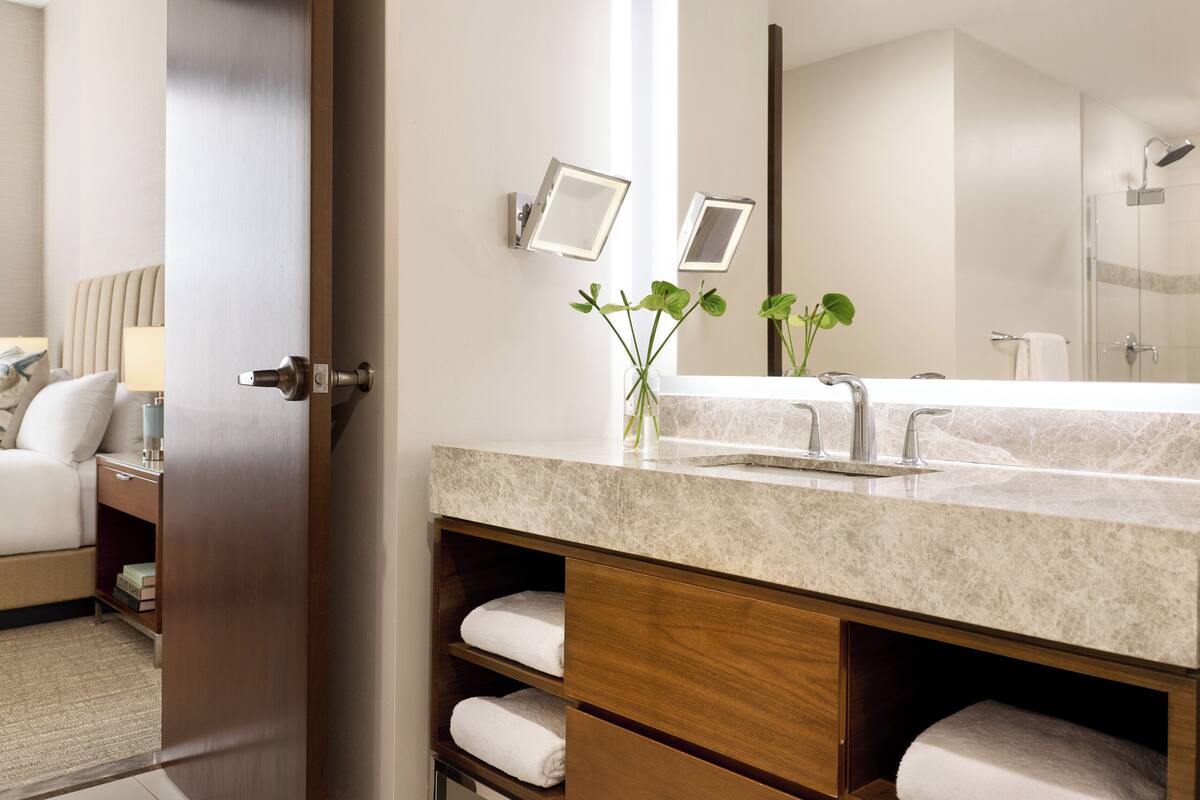A bathroom with a marble sink, two framed mirrors, a shower, and a towel rack.