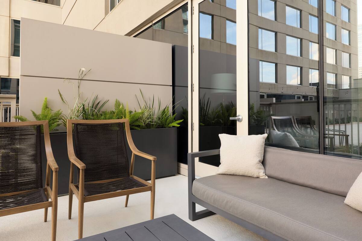 A modern outdoor seating area with a sofa and chairs, a potted plant, and a view of a building.
