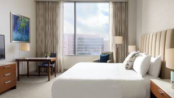 A hotel room with a large bed, a desk, a chair, a TV, and a window with curtains.