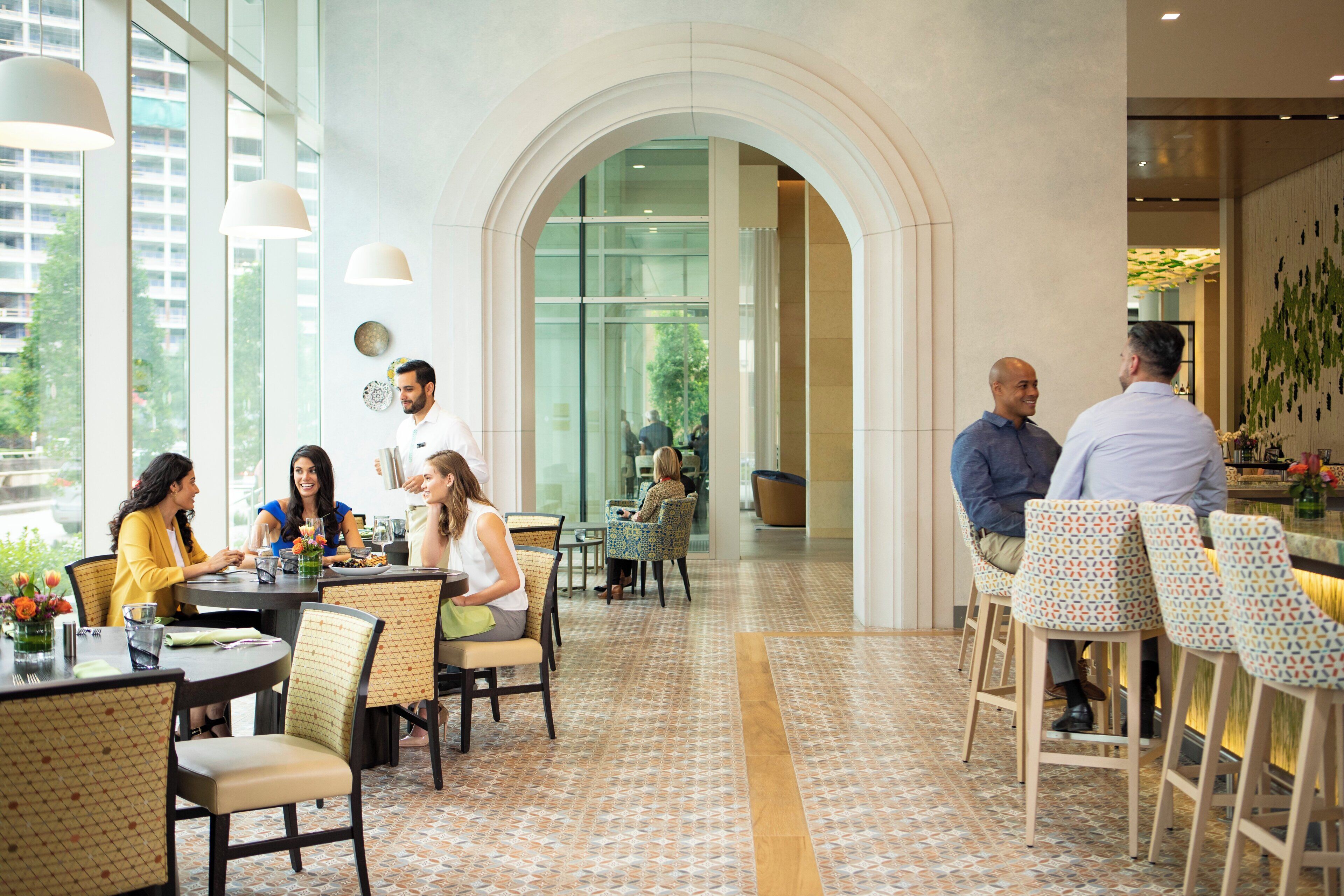 Un comedor moderno con techos altos, ventanas amplias y una variedad de disposiciones de asientos que incluyen mesas y sillas.