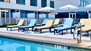A poolside area with lounge chairs and umbrellas, a clear pool, and a modern building in the background. - InterContinental Houston by IHG (Houston)