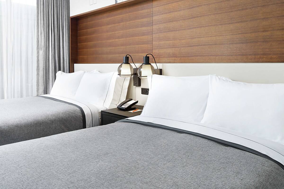 A hotel room with two beds, a wooden headboard, bedside lamps, a nightstand, and a telephone.