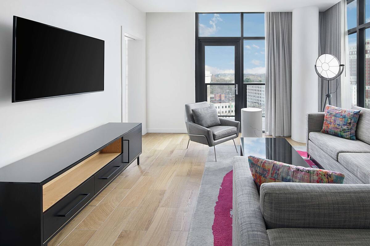 A modern living room with a flat-screen TV, grey sofa, armchair, and a coffee table.