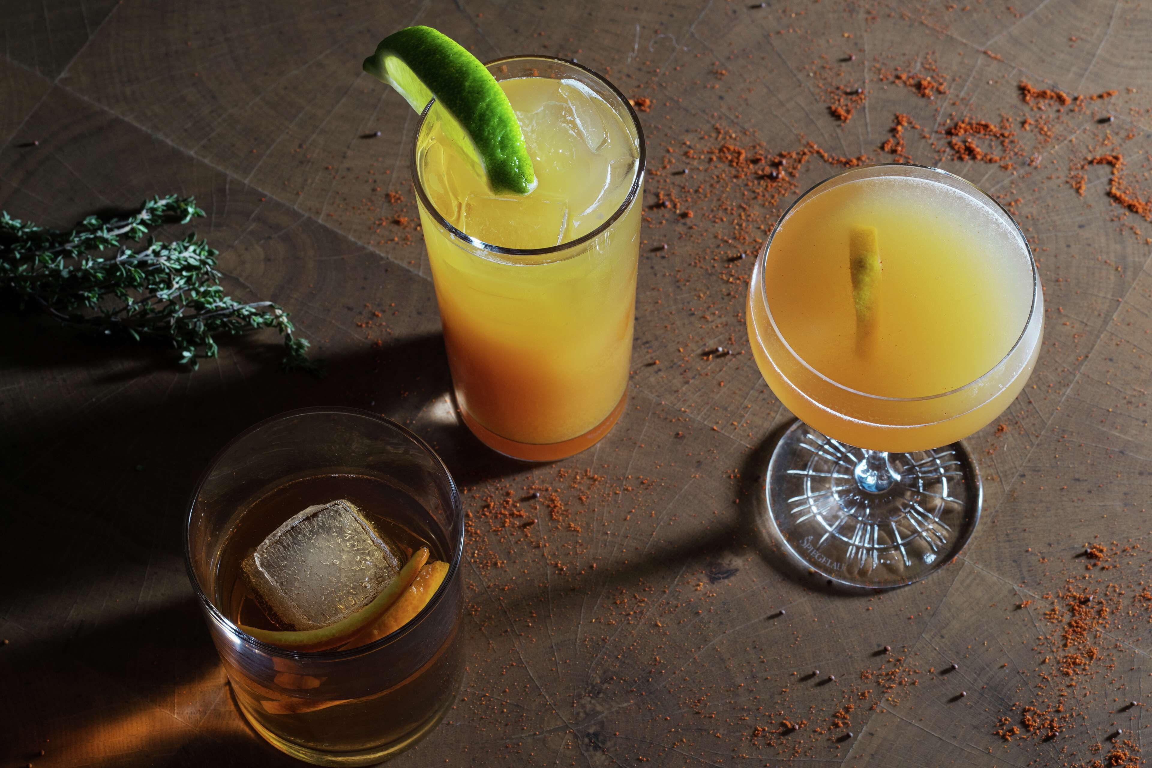 Tres vasos de bebidas sobre una superficie texturizada, con especias dispersas.