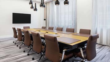 A conference room with a long table, brown leather chairs, and a flat-screen TV on the wall.