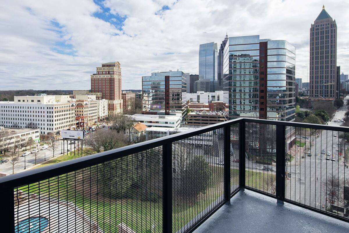 A cityscape with modern buildings, a parking lot, and a fenced balcony.
