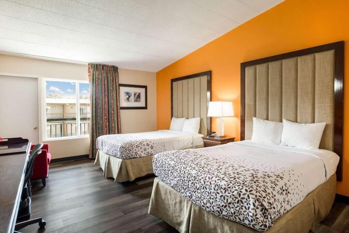A hotel room with two beds, a desk, a chair, a window with curtains, and a balcony view.