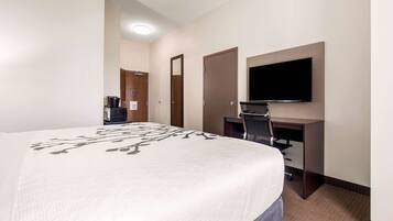 Quarto de hotel com uma cama grande, uma escrivaninha com televisão de tela plana, uma cafeteira e uma porta.