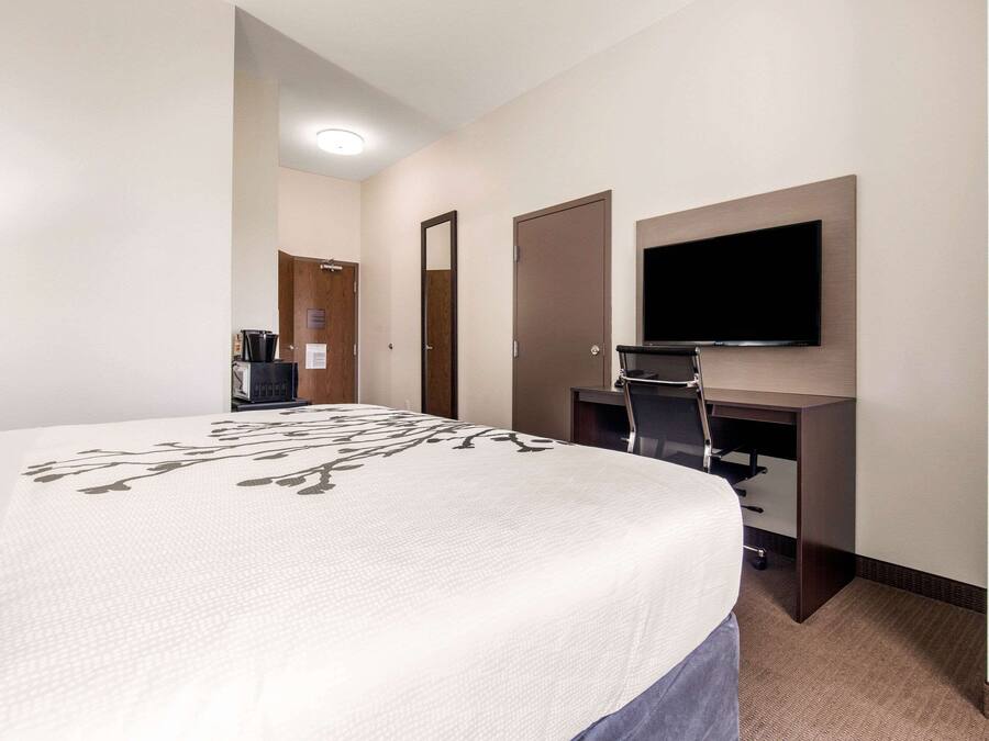 Quarto de hotel com uma cama grande, uma escrivaninha com televisão de tela plana, uma cafeteira e uma porta.