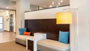A modern hotel lobby with a seating area featuring a sofa and a small table, a large floor lamp, and an elevator in the background. - Sleep Inn & Suites South Jacksonville (Jacksonville)