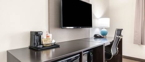 Hotelkamer met een flatscreen televisie aan de muur, een bureau met een koffiezetapparaat, een magnetron en een stoel.