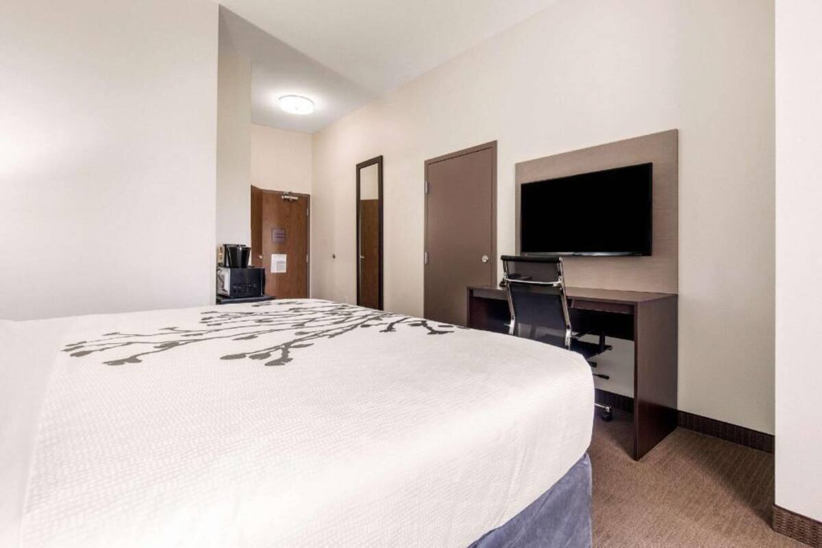 A hotel room with a large bed, a desk with a flat-screen TV, a coffee machine, and a door.