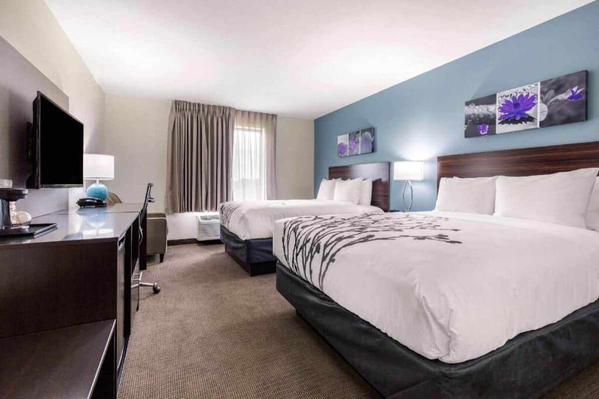 A hotel room with two beds, a desk, a TV, and artwork on the walls.