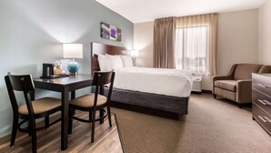 A hotel room with a bed, a desk with chairs, a dresser, and a window with curtains. - Sleep Inn & Suites South Jacksonville (Jacksonville)