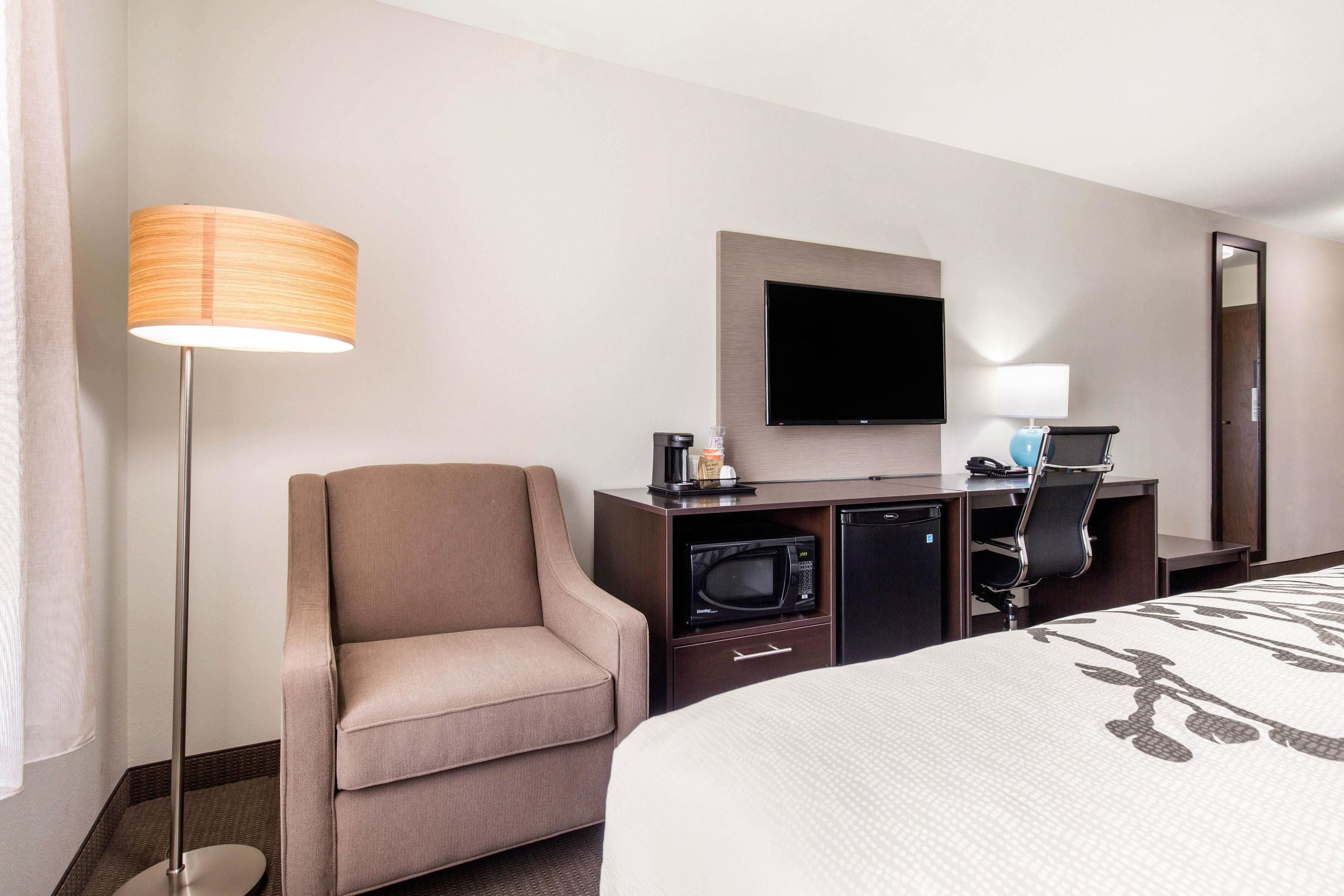 Habitación de hotel con cama, escritorio con televisor de pantalla plana, microondas, cafetera y una silla.