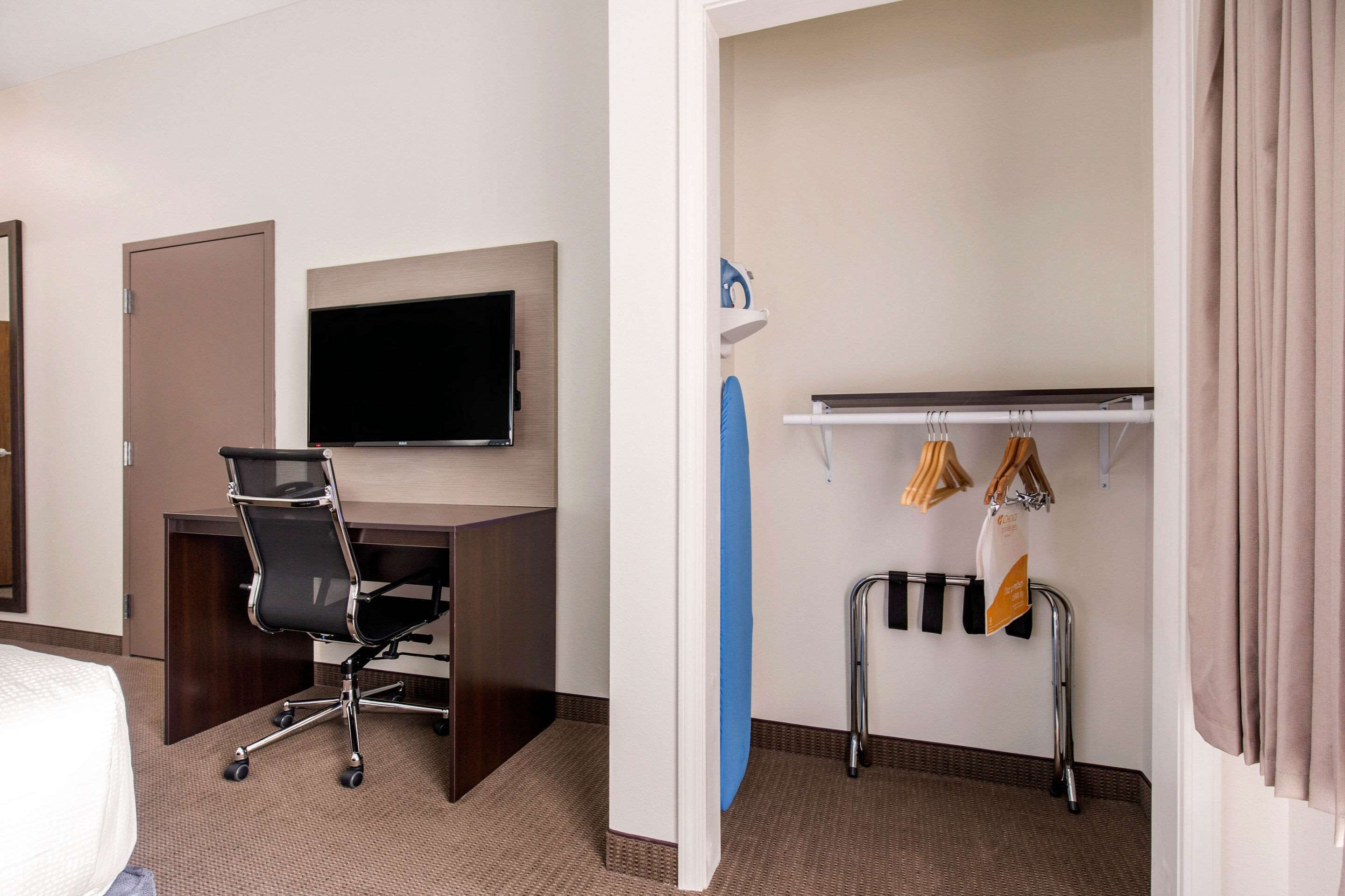A hotel room with a desk, chair, television, and a coat rack with hangers.