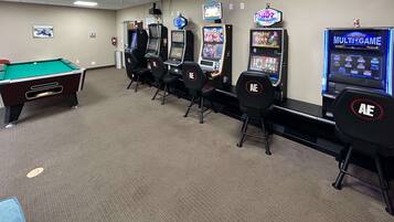 A room with a pool table, several gaming machines, and chairs.