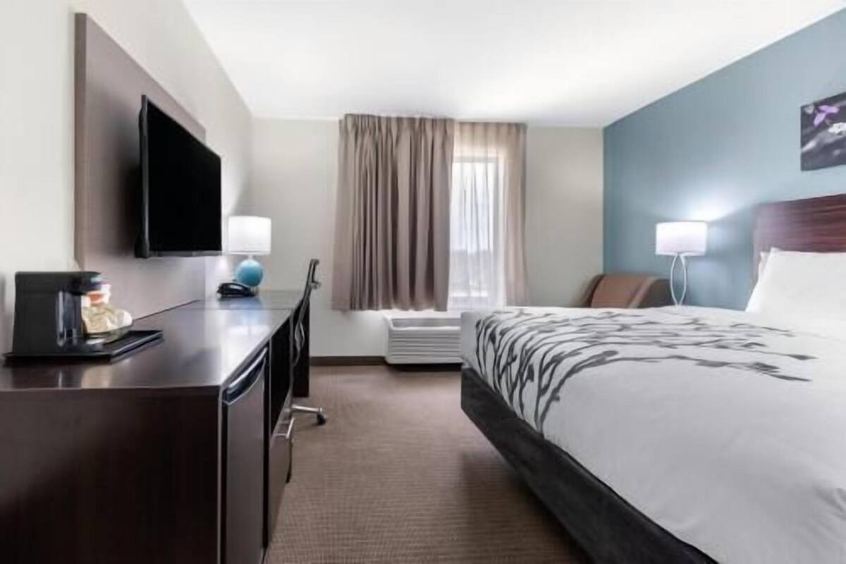 A hotel room with a bed, a desk, a television, a lamp, and a window with curtains.