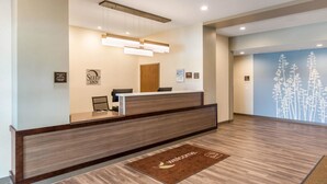 A reception area with a wooden reception desk, a 'Welcome' mat, and a wall-mounted sign. - Sleep Inn & Suites South Jacksonville (Jacksonville)