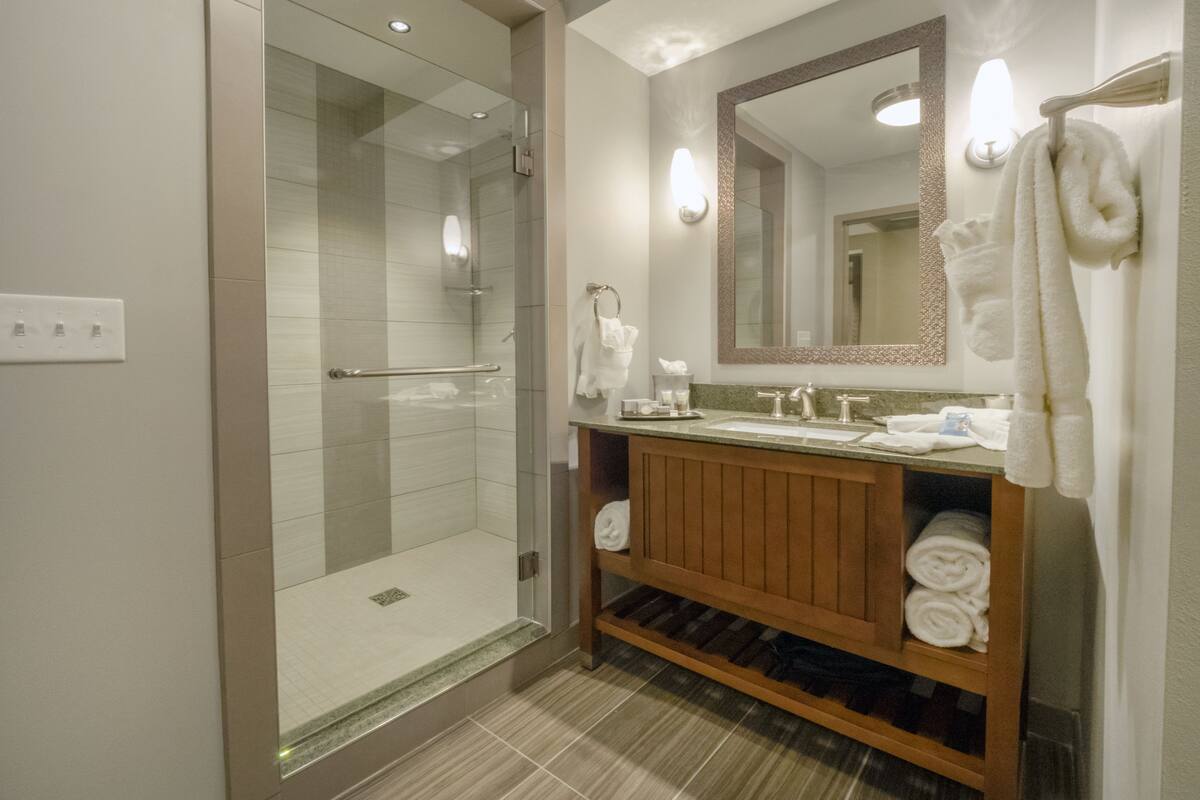 Un baño moderno con ducha de vidrio, tocador de madera con lavamanos y un espejo grande.