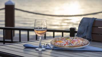 Una pizza y una copa de vino sobre una mesa con vistas al agua.
