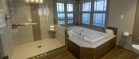 A modern bathroom with a glass-enclosed shower, a large bathtub, and a view of the sea through large windows.