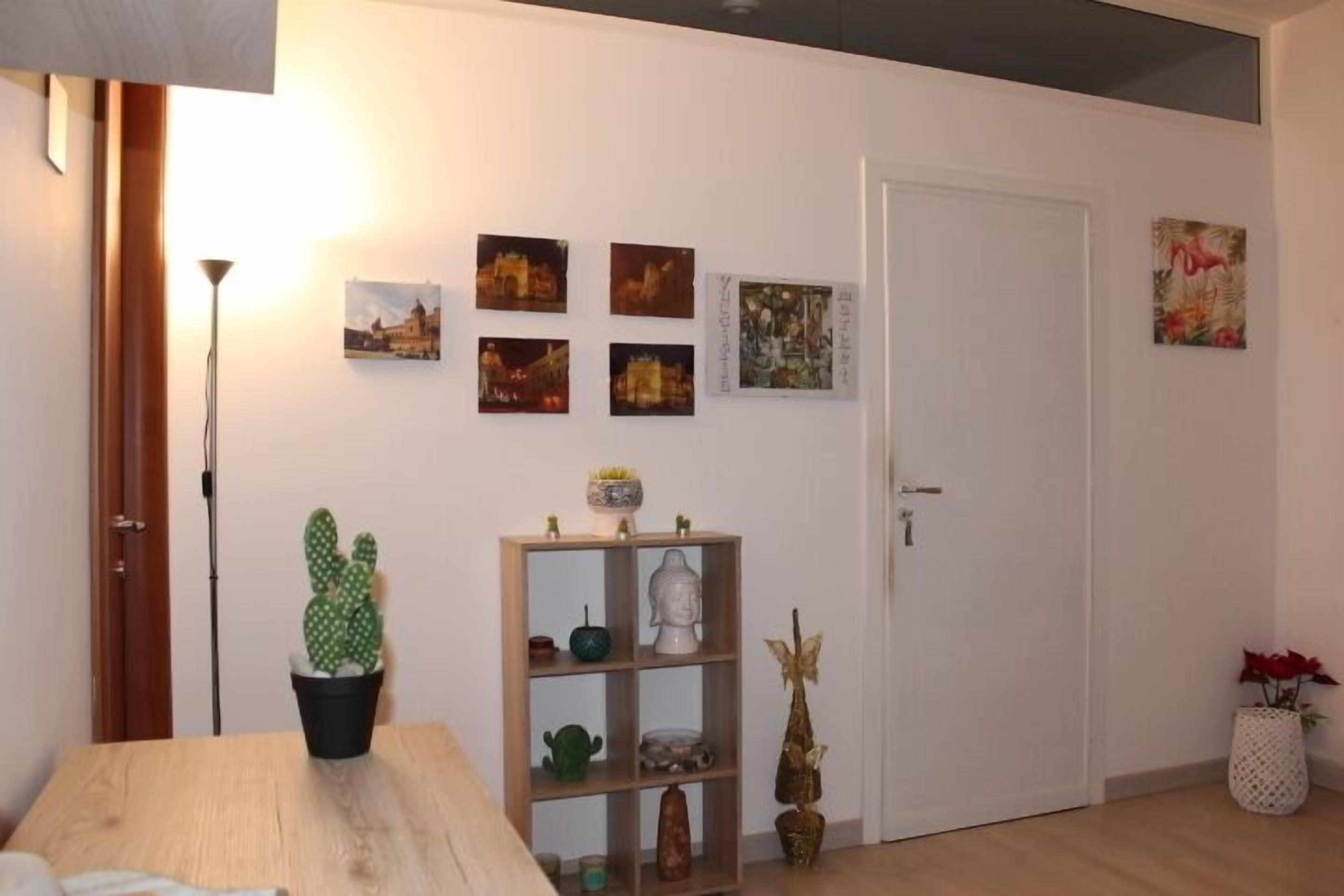 Una habitación con una mesa de madera, una planta de cactus, un estante con adornos y una puerta.