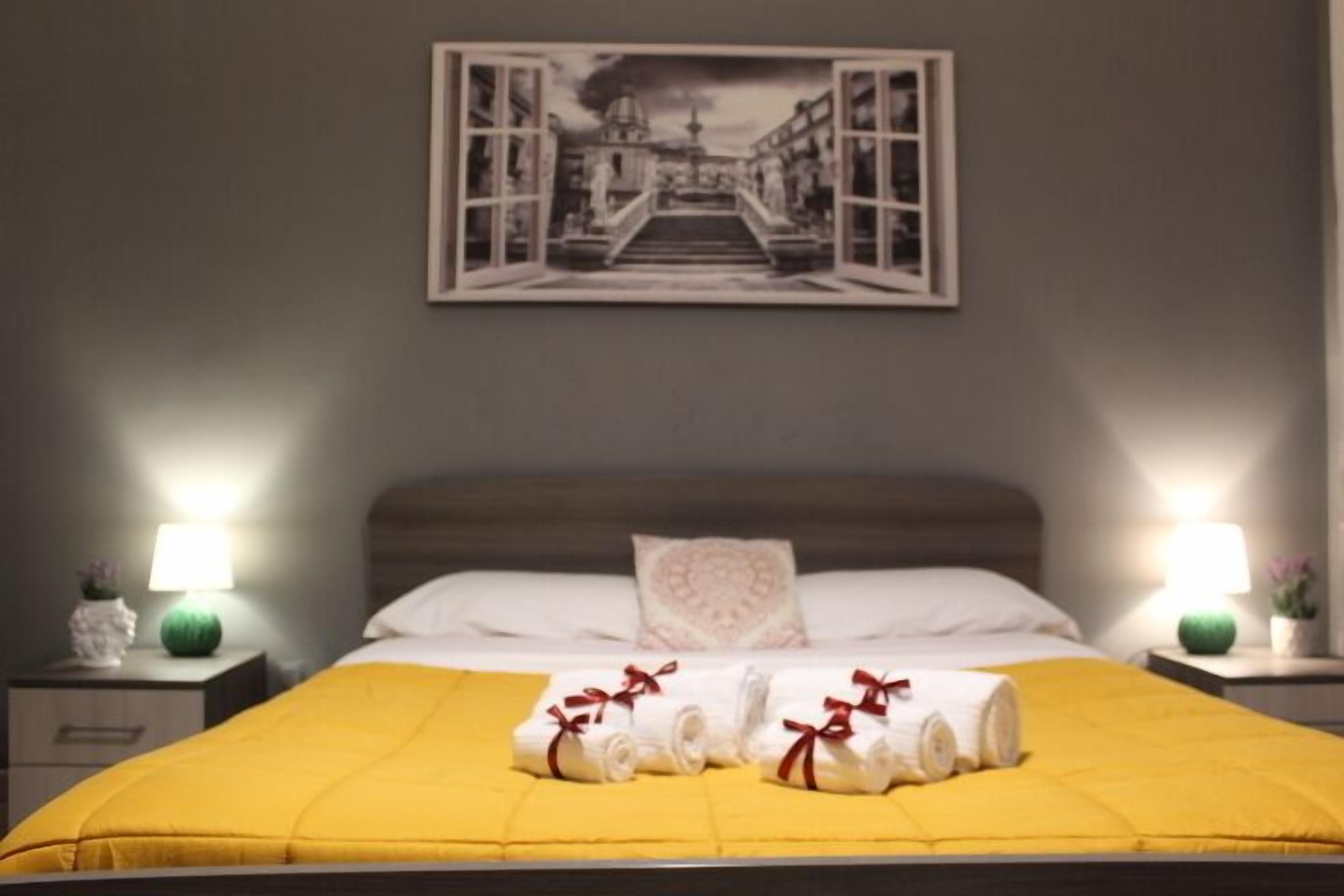 A hotel room with a bed, two bedside lamps, a painting on the wall, and towels on the bed.