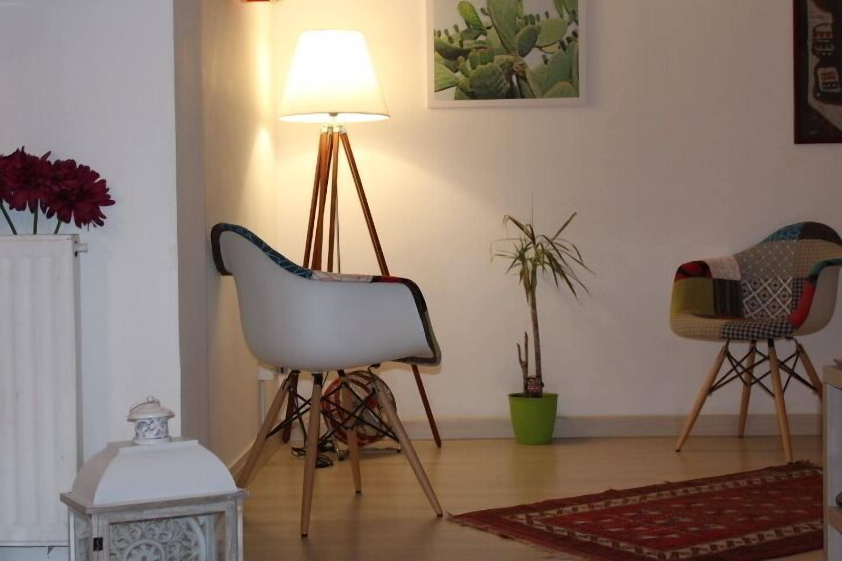 Un salon avec un fauteuil blanc, une lampe sur pied, un cactus et une chaise aux couleurs vives.