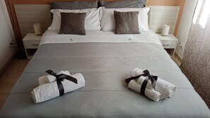 A neatly made bed with two towels tied with black ribbons, a grey headboard, and a bedside table with a lamp. - Dante091 (Palermo)