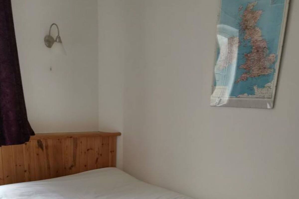 A single bed with a white sheet in a room with wooden headboard and a map on the wall.