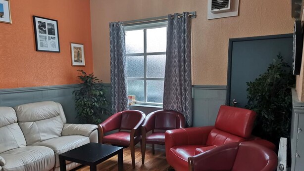 A living room with a beige sofa, two red armchairs, a small black table, and a window with curtains. - Swan Inn, Heathrow Airport (Staines)