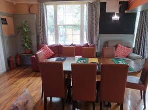 A cozy dining area with a wooden table and matching chairs, a sofa with red cushions, and a potted plant. - Swan Inn, Heathrow Airport (Staines)