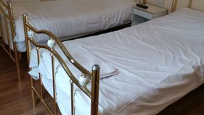 A room with two single beds, wooden headboards, a bedside table with a lamp, and a radiator on the wall. - Swan Inn, Heathrow Airport (Staines)