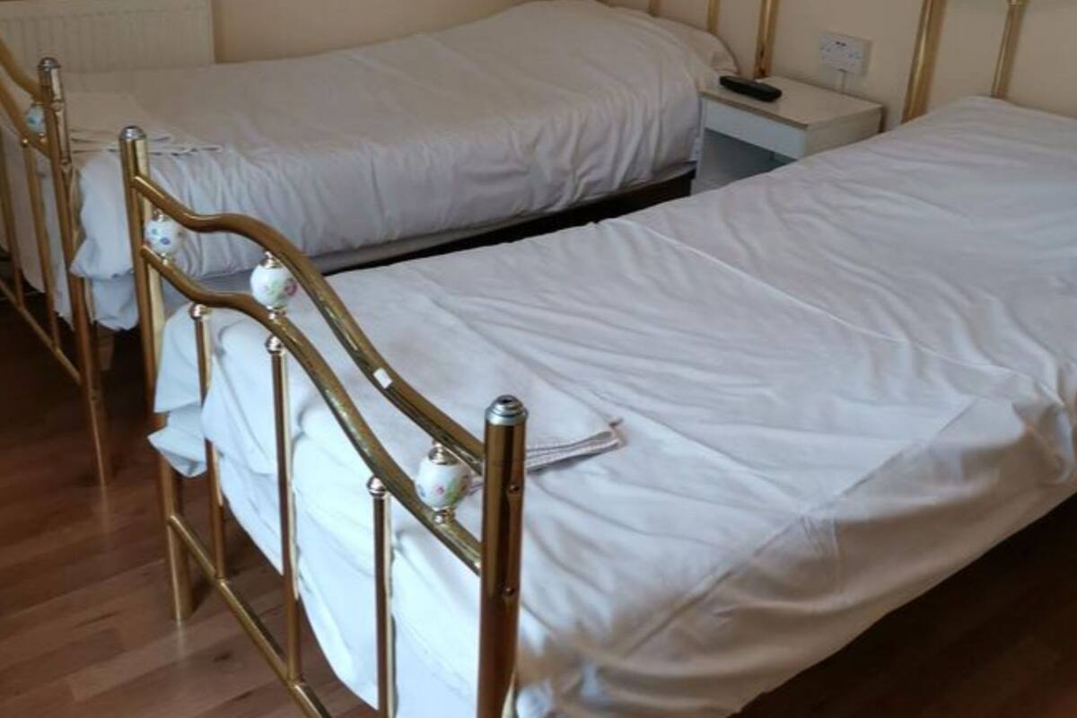 A room with two single beds, wooden headboards, a bedside table with a lamp, and a radiator on the wall.