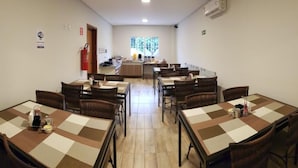 Un comedor con manteles a cuadros, sillas de mimbre y una cocina al fondo.