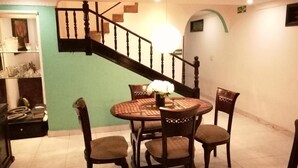 A dining area with a round table, four chairs, and a vase with flowers. A staircase with a wooden railing is visible in the background. - Taminaka Hostel (Santa Marta)