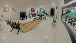 A spacious living room with a sofa, chairs, a TV, and a dining area with a staircase. - Taminaka Hostel (Santa Marta)