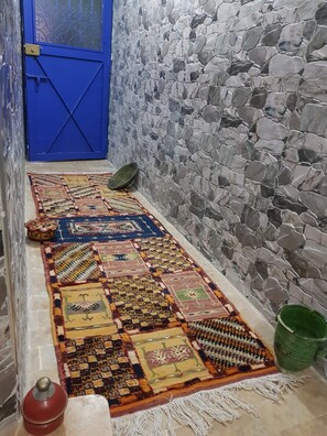 A narrow hallway with a blue door, a stone wall, and a patterned rug. - Sun Hostel Marrakech (Marrakech)