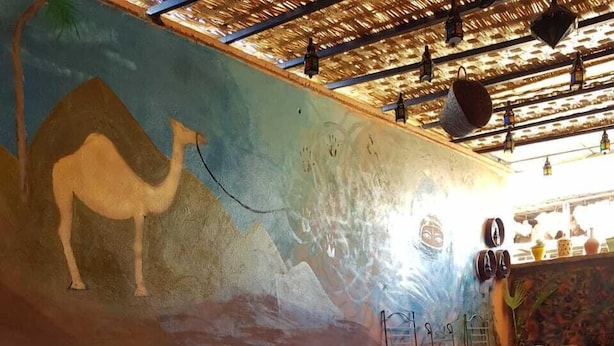 A cozy lounge area with a colorful mural, a sofa set, wooden tables, and a patterned floor. - Sun Hostel Marrakech (Marrakech)