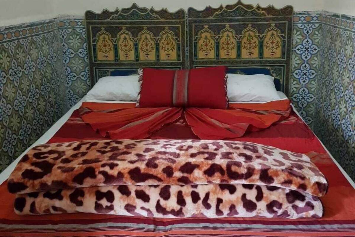 Una cama con una manta de estampado de leopardo, almohadas rojas y un cubrecolchón rojo.