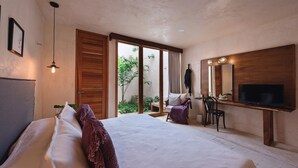A bedroom with a large bed, a desk with a chair, a TV, and a sliding glass door leading to a garden. - Colonte Hotel Origen (Valladolid)