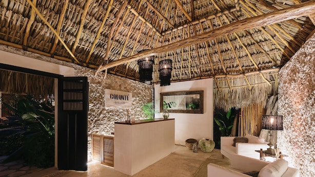 A reception area with a thatched roof, a reception desk, a sofa, and a wall-mounted lamp. - Colonte Hotel Origen (Valladolid)