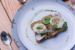 A plate with a sandwich topped with avocado, radish, and a poached egg, garnished with cilantro and black pepper. - Colonte Hotel Origen (Valladolid)