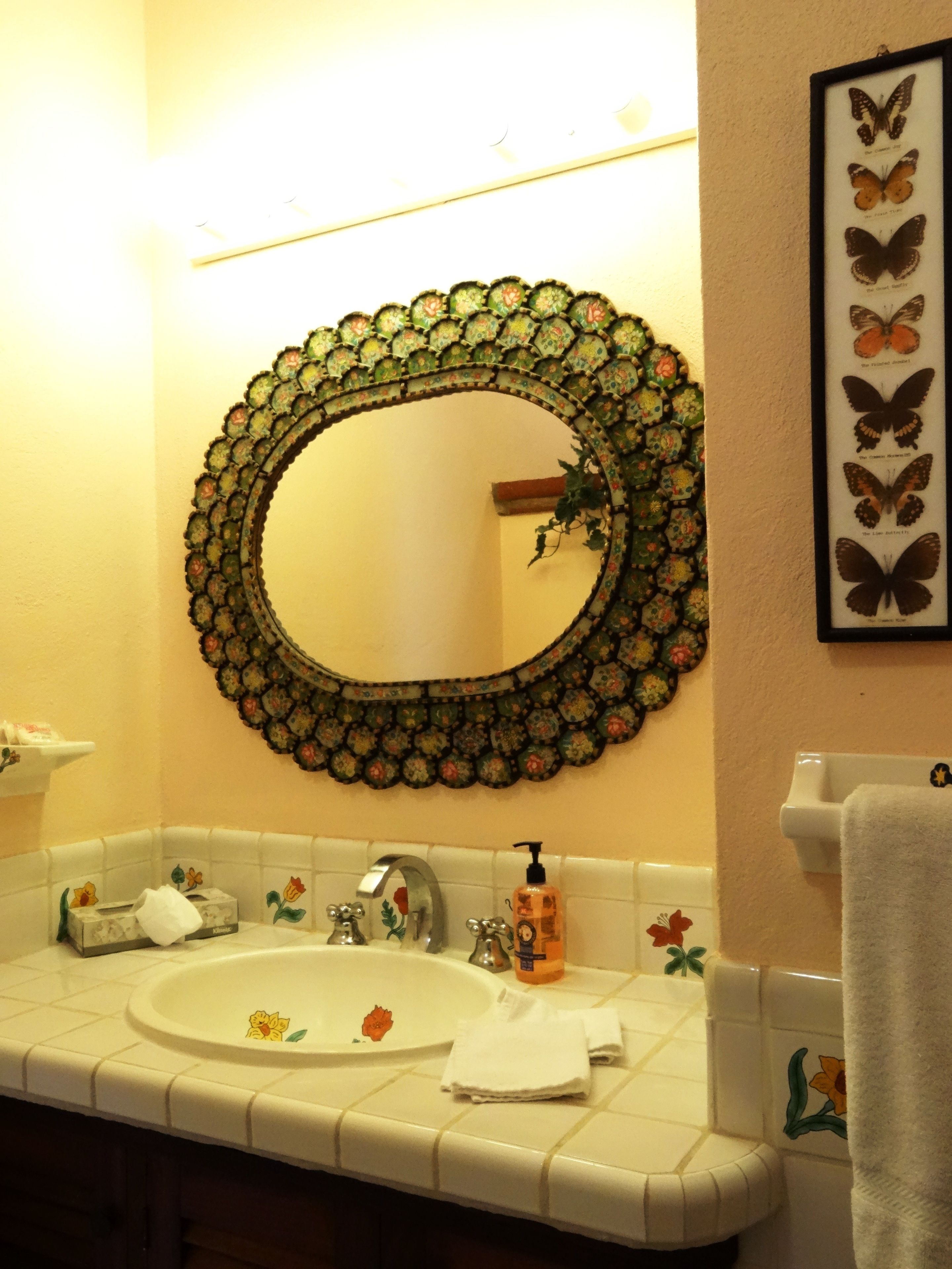 Een badkamer met een ronde spiegel, een wastafel en een wanddecoratie met vlinders.