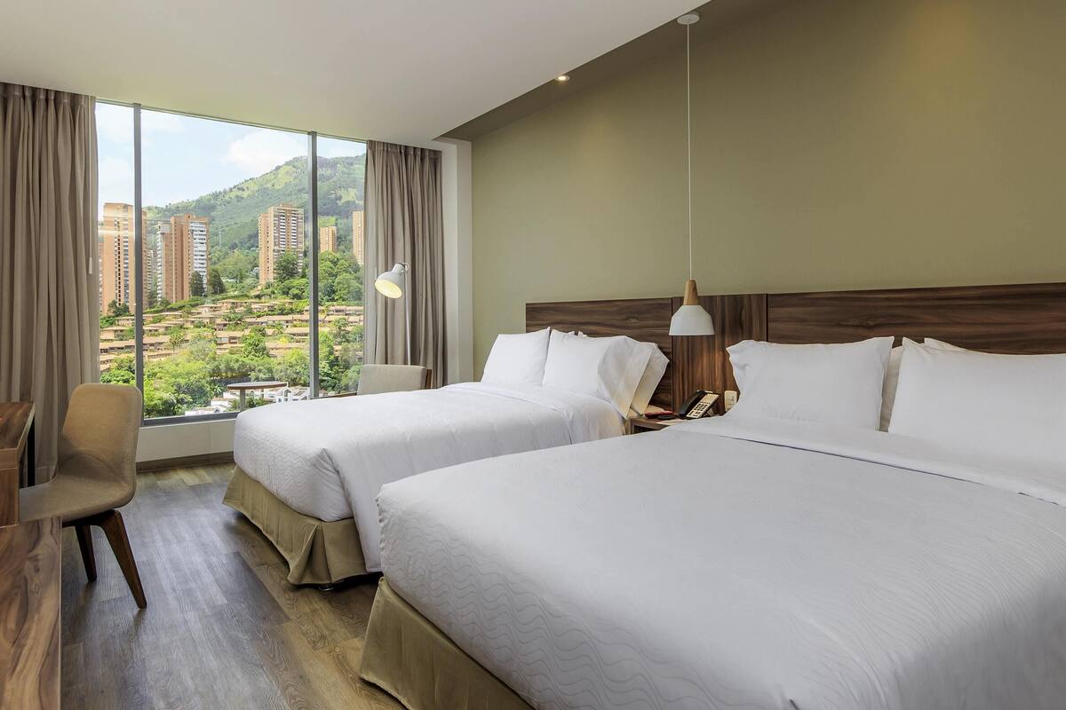 Une chambre d’hôtel avec deux lits, un bureau et une vue sur des immeubles et des espaces verts.